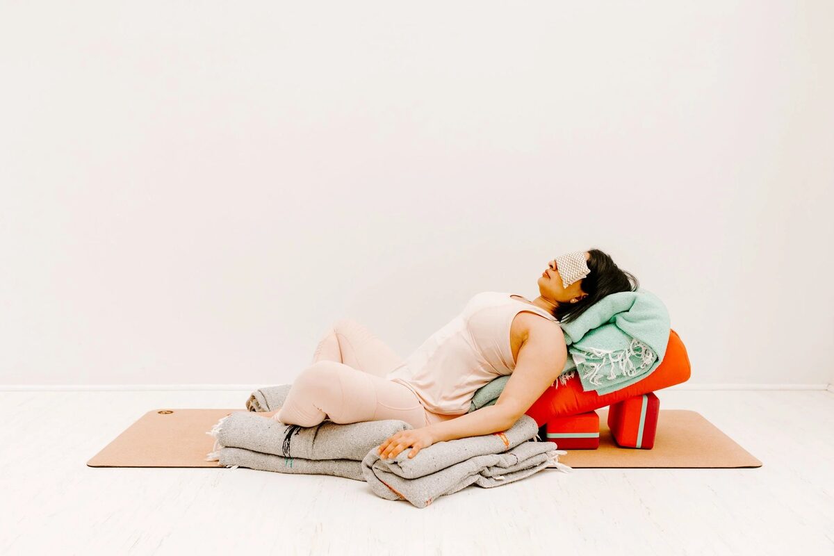 A student resting in a supported reclining pose over a bolster, fully at ease.